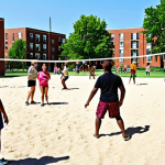**A vibrant, diverse community playing volleyball in a park on a sunny day. Show people of all ages and backgrounds laughing and interacting while playing. In the background, depict apartment buildings to emphasize the neighborhood setting and sense of community.**